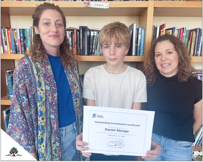 Daniel Abrego, alumno del Colegio Juan de Lanuza, posa con su certificado de reconocimiento de Fiction Express junto a dos profesoras en la biblioteca del centro.