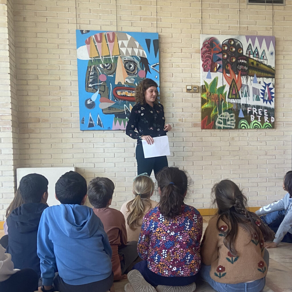 Profesora del Colegio Juan de Lanuza presenta la exposición «Remyland» ante alumnos en el hall del centro.