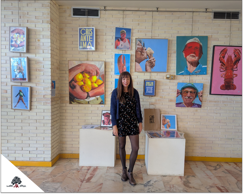 La artista Crisantelma posa en los pasillos del Colegio Juan de Lanuza frente a una exposición de retratos coloridos que combinan arte y tecnología.